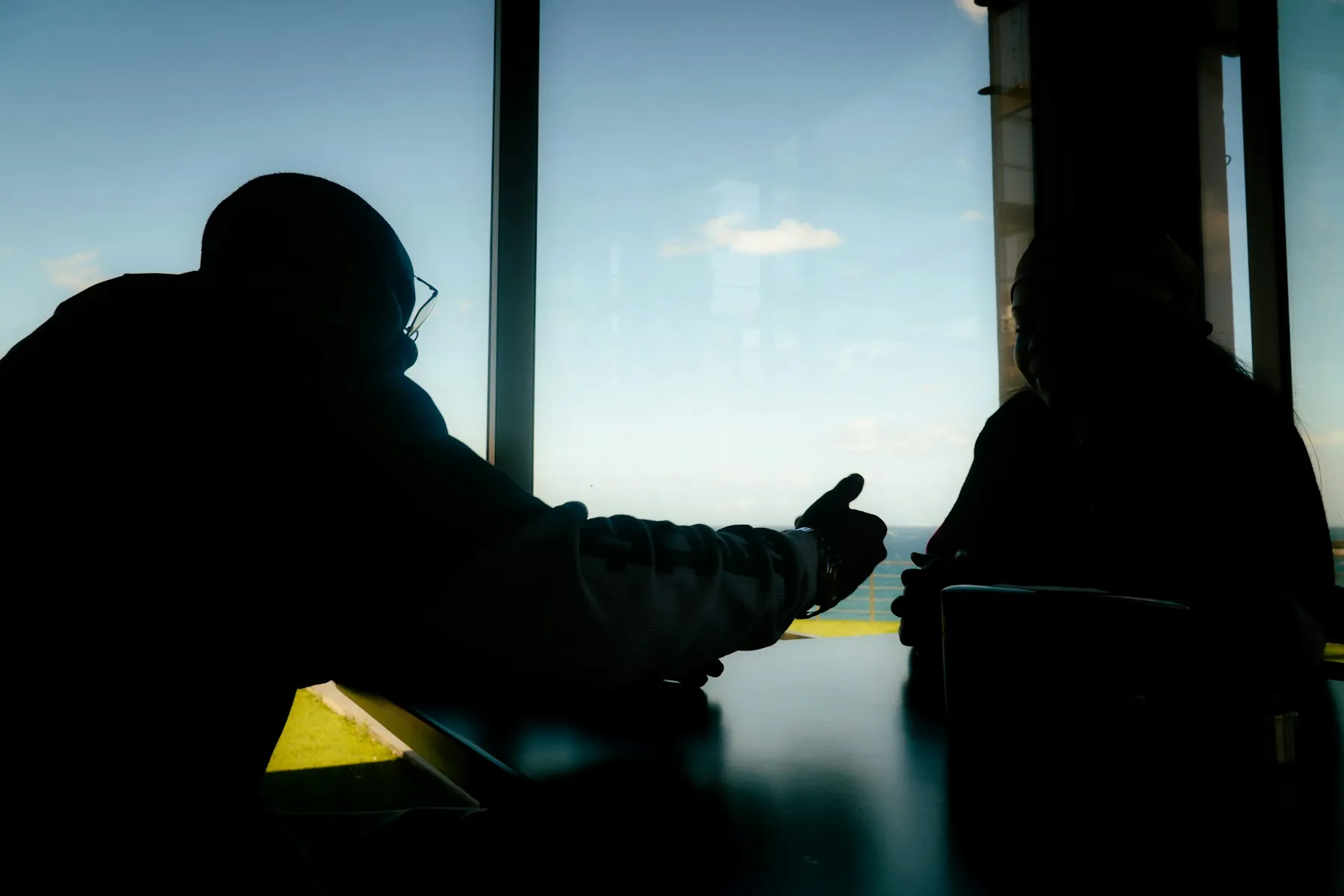 Silhouetten zweier Menschen an einem Tisch vor einem Fenster