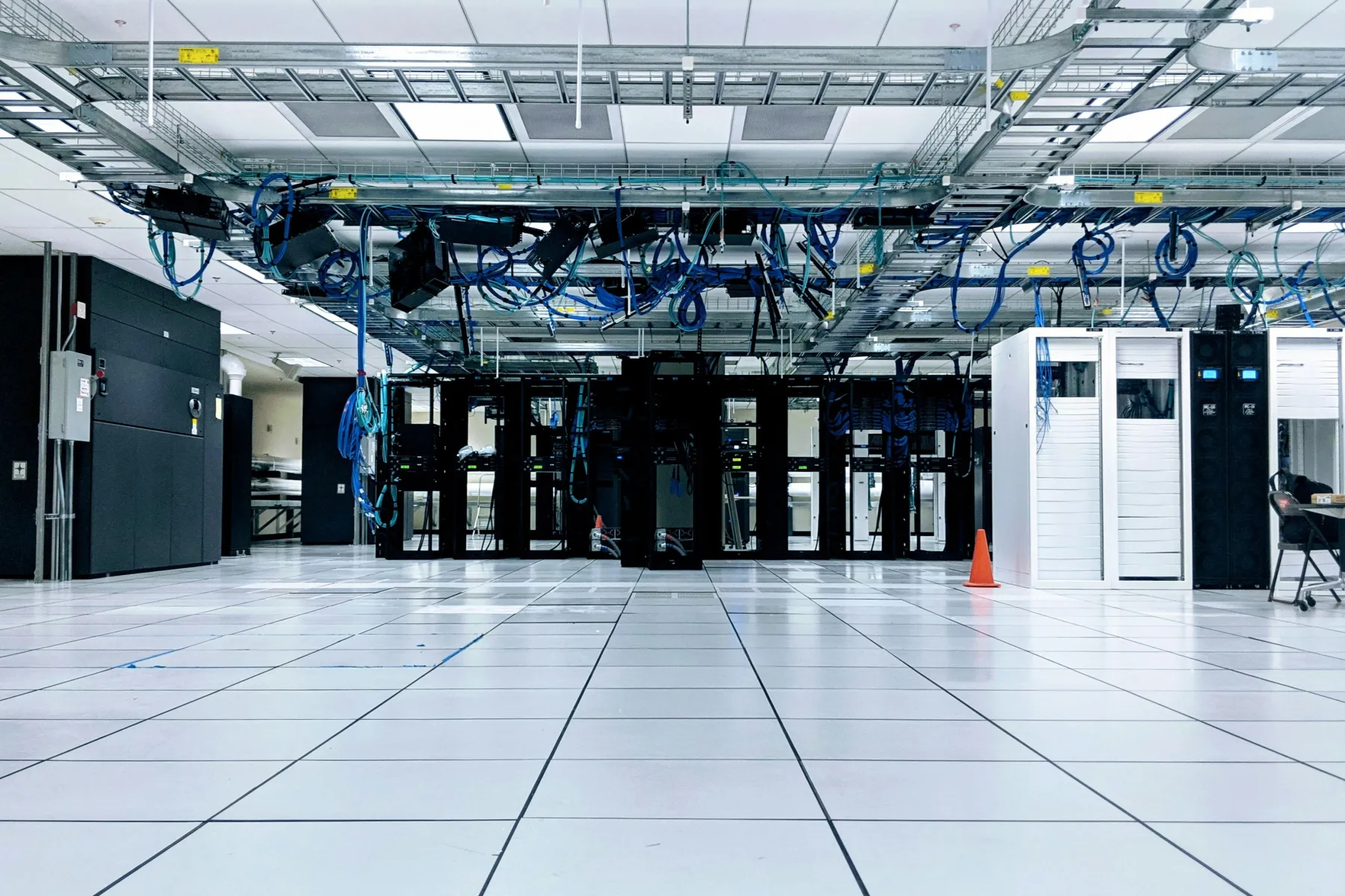 Ein leerer Serverraum mit schwarzen und weißen Schränken, darüber Kabeltrassen mit blauen Netzwerkkabeln