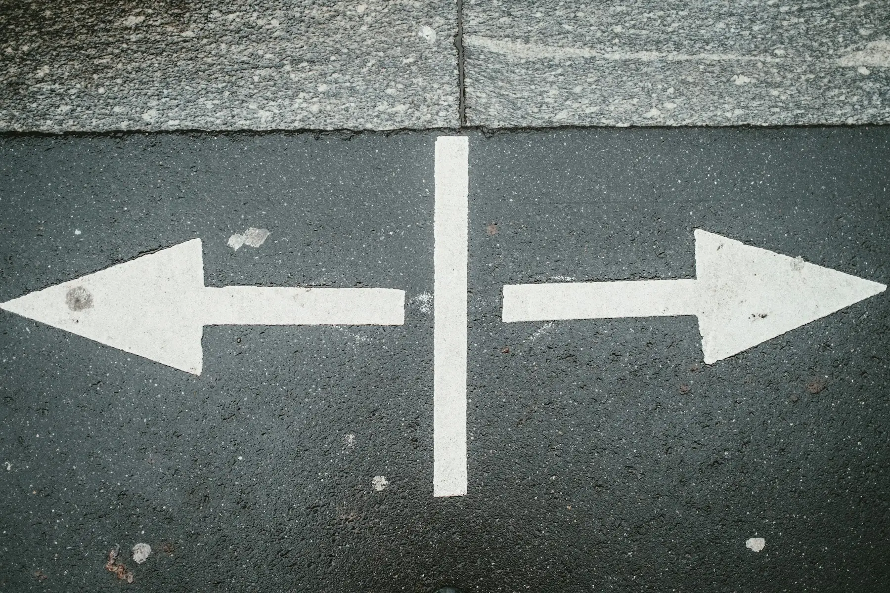 Zwei weiße Pfeile auf Asphalt, die in entgegengesetzte Richtungen zeigen